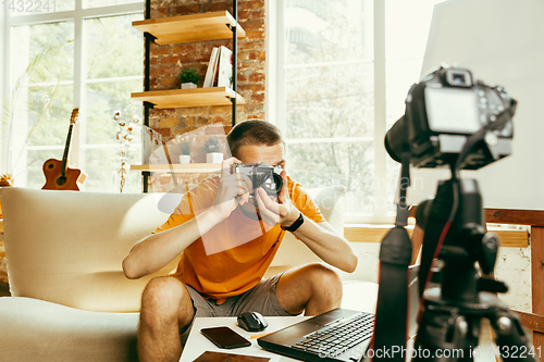 Image of Caucasian male blogger with camera recording video review of gadgets at home