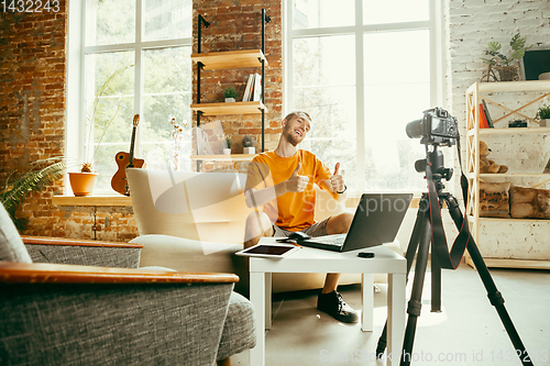 Image of Caucasian male blogger with camera recording video review of gadgets at home