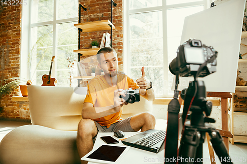 Image of Caucasian male blogger with camera recording video review of gadgets at home