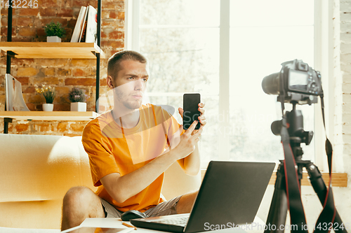 Image of Caucasian male blogger with camera recording video review of gadgets at home