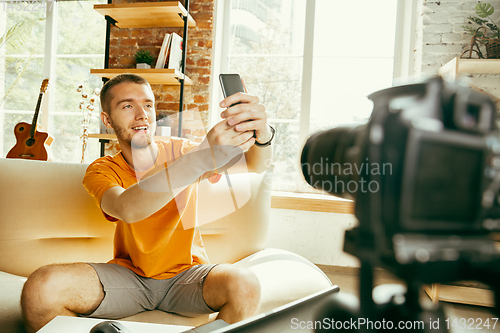 Image of Caucasian male blogger with camera recording video review of gadgets at home