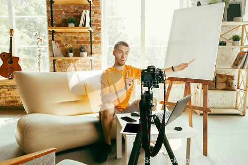 Image of Caucasian male blogger with camera recording video review of gadgets at home