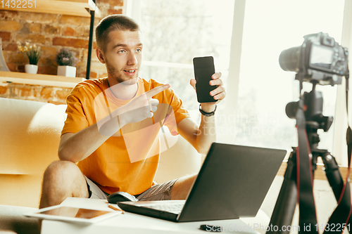 Image of Caucasian male blogger with camera recording video review of gadgets at home