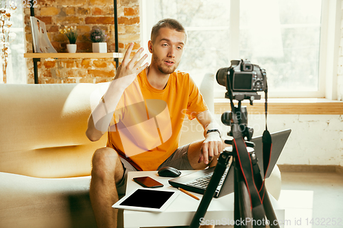 Image of Caucasian male blogger with camera recording video review of gadgets at home