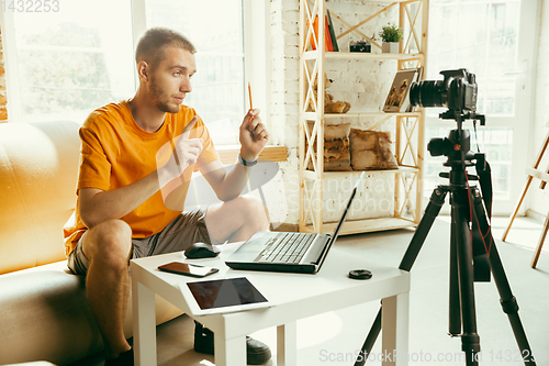 Image of Caucasian male blogger with camera recording video review of gadgets at home