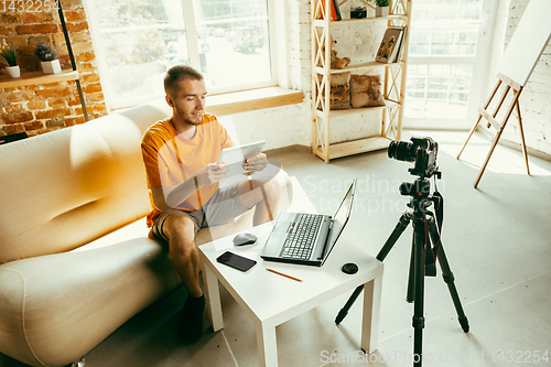 Image of Caucasian male blogger with camera recording video review of gadgets at home