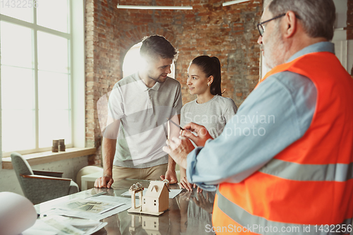 Image of Foreman or achitect shows house, office or store design plans to a young couple