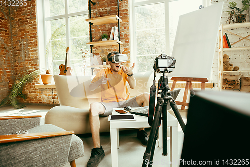 Image of Caucasian male blogger with camera recording video review of gadgets at home