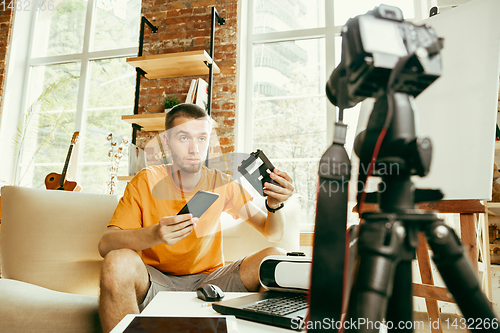 Image of Caucasian male blogger with camera recording video review of gadgets at home