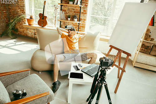 Image of Caucasian male blogger with camera recording video review of gadgets at home