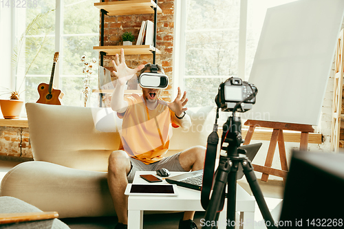 Image of Caucasian male blogger with camera recording video review of gadgets at home