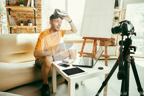 Image of Caucasian male blogger with camera recording video review of gadgets at home