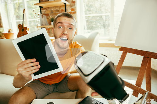 Image of Caucasian male blogger with camera recording video review of gadgets at home