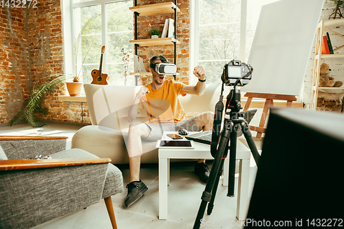 Image of Caucasian male blogger with camera recording video review of gadgets at home