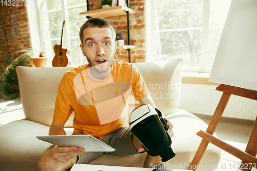 Image of Caucasian male blogger with camera recording video review of gadgets at home