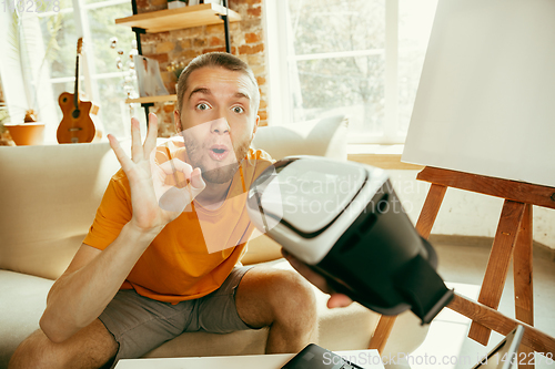 Image of Caucasian male blogger with camera recording video review of gadgets at home