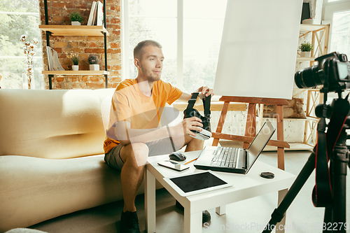 Image of Caucasian male blogger with camera recording video review of gadgets at home