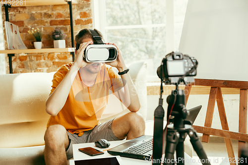 Image of Caucasian male blogger with camera recording video review of gadgets at home