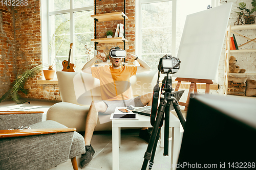 Image of Caucasian male blogger with camera recording video review of gadgets at home