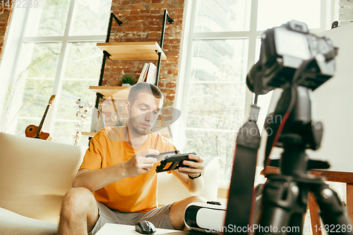 Image of Caucasian male blogger with camera recording video review of gadgets at home