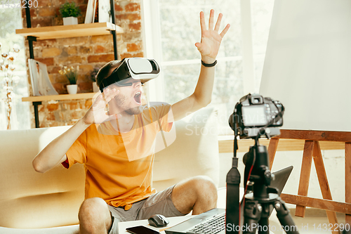 Image of Caucasian male blogger with camera recording video review of gadgets at home