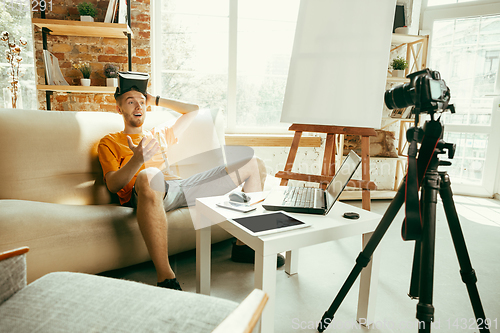 Image of Caucasian male blogger with camera recording video review of gadgets at home