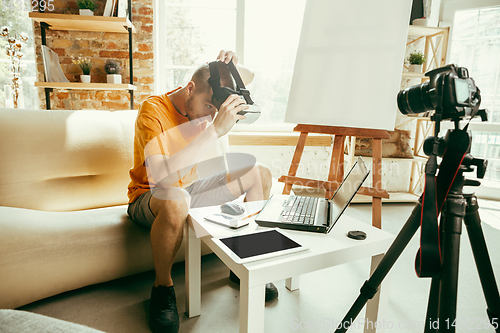 Image of Caucasian male blogger with camera recording video review of gadgets at home