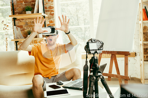 Image of Caucasian male blogger with camera recording video review of gadgets at home