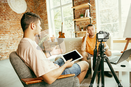 Image of Two young male bloggers with professional camera recording video interview at home