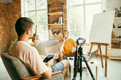 Image of Two young male bloggers with professional camera recording video interview at home