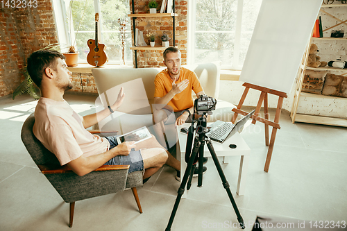 Image of Two young male bloggers with professional camera recording video interview at home