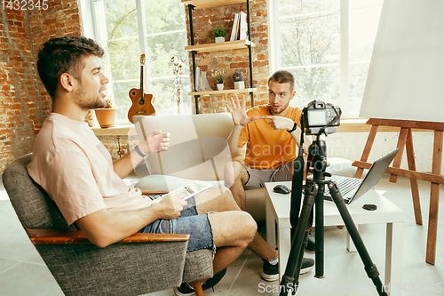 Image of Two young male bloggers with professional camera recording video interview at home