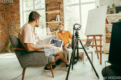 Image of Two young male bloggers with professional camera recording video interview at home