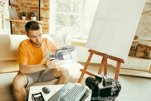 Image of Caucasian male blogger with camera recording video review of gadgets at home