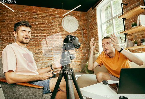 Image of Two young male bloggers with professional camera recording video interview at home