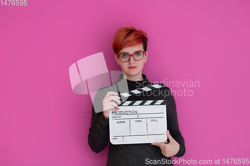 Image of redhead woman holding movie  clapper on pink background