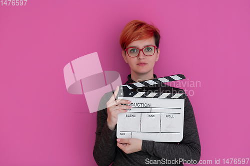 Image of redhead woman holding movie  clapper on pink background