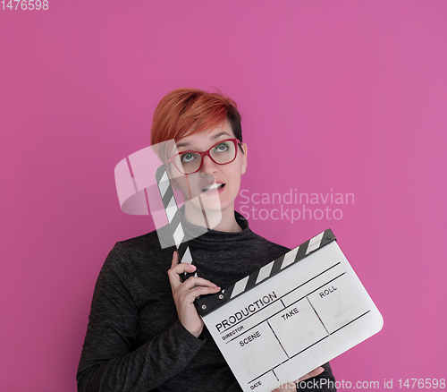 Image of redhead woman holding movie  clapper on pink background