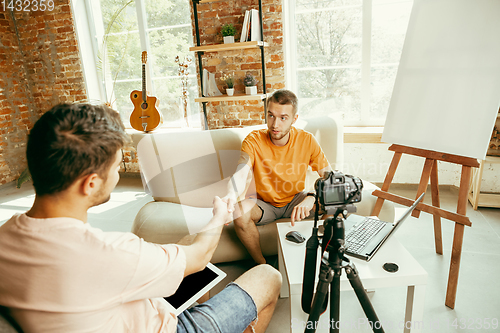 Image of Two young male bloggers with professional camera recording video interview at home