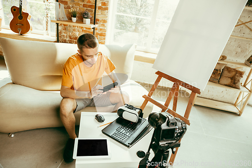 Image of Caucasian male blogger with camera recording video review of gadgets at home