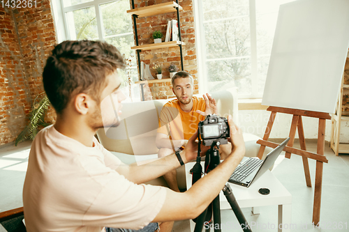 Image of Two young male bloggers with professional camera recording video interview at home