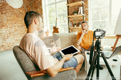 Image of Two young male bloggers with professional camera recording video interview at home