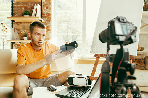 Image of Caucasian male blogger with camera recording video review of gadgets at home