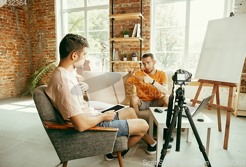 Image of Two young male bloggers with professional camera recording video interview at home