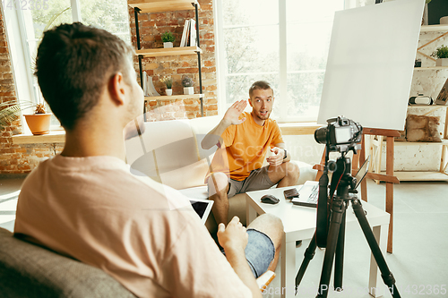 Image of Two young male bloggers with professional camera recording video interview at home