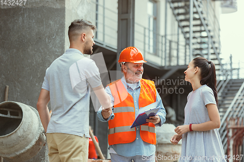 Image of Foreman or achitect shows house, office or store design plans to a young couple