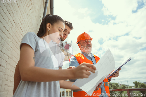 Image of Foreman or achitect shows house, office or store design plans to a young couple