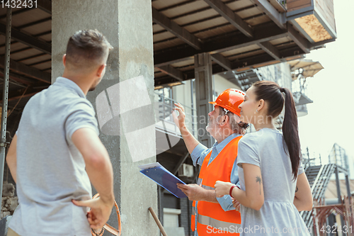 Image of Foreman or achitect shows house, office or store design plans to a young couple