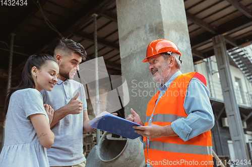 Image of Foreman or achitect shows house, office or store design plans to a young couple