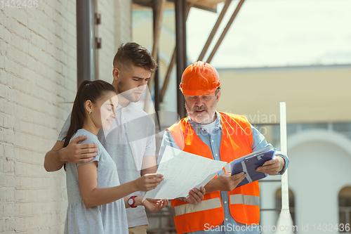 Image of Foreman or achitect shows house, office or store design plans to a young couple